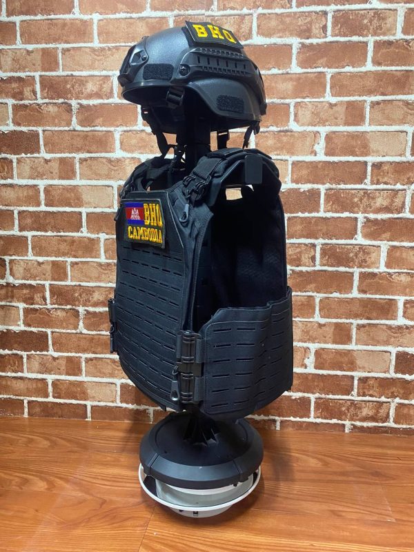 Black tactical vest with patches and helmet on display stand.