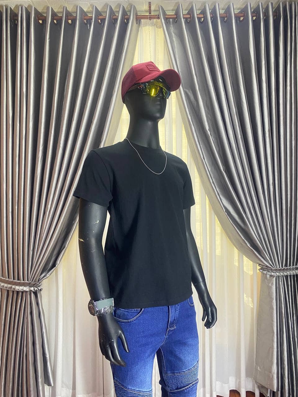 Black t-shirt, red cap, yellow sunglasses, and blue jeans on mannequin.