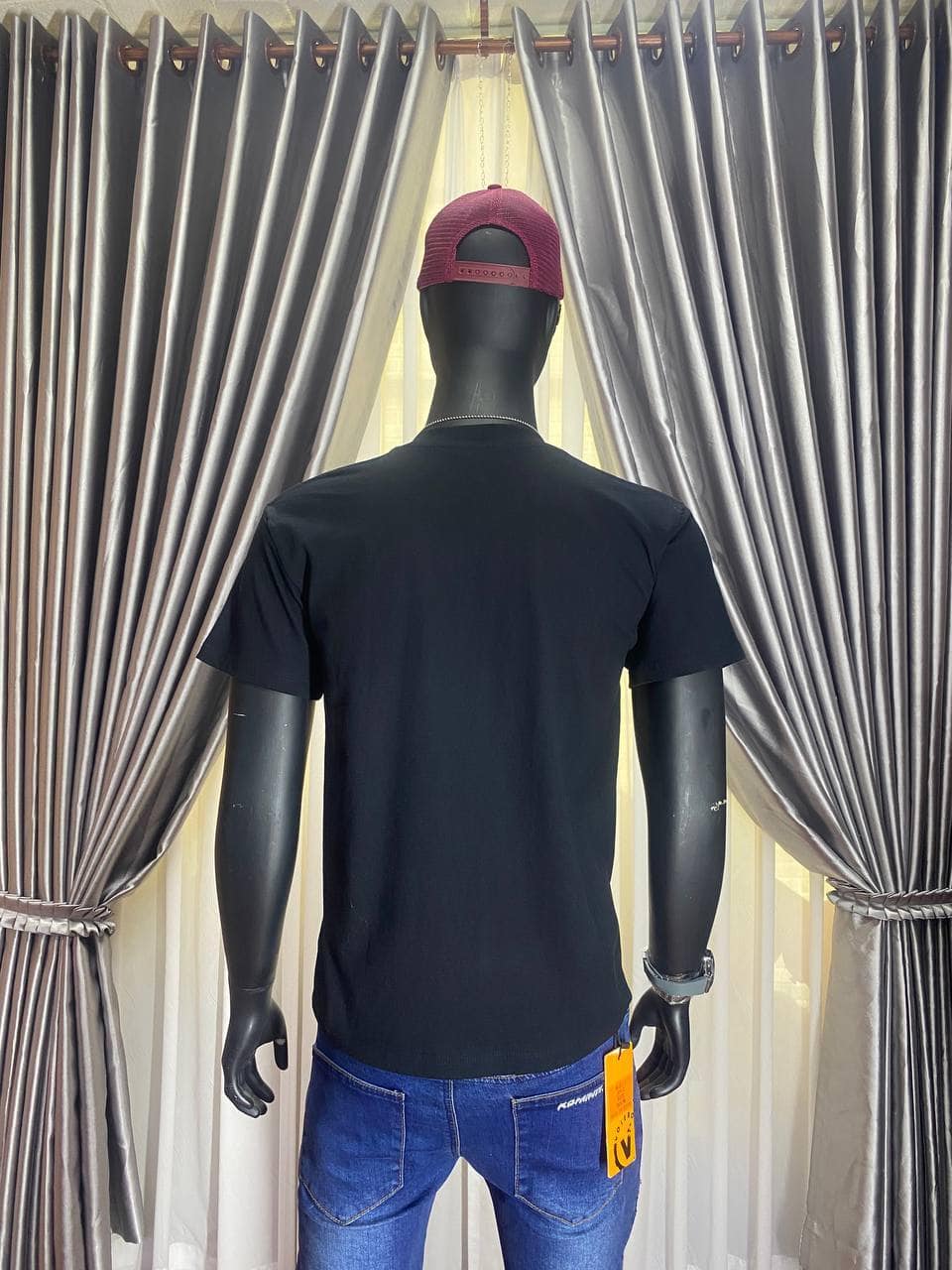 Black t-shirt on mannequin with red cap in front of curtains.