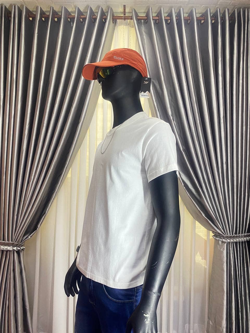 Orange cap with black sunglasses on a mannequin in white T-shirt.