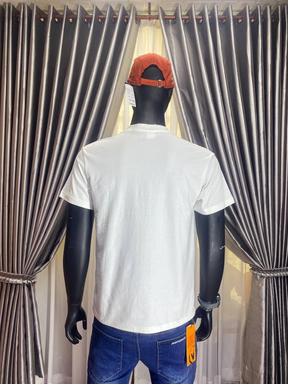 Orange cap on mannequin, white T-shirt, blue jeans, in store display.